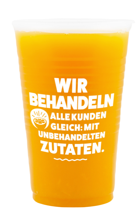 Becher mit Orangensaft von Campus Suite mit der Aufschrift "Wir behandeln alle Kunden gleich: mit unbehandelten Zutaten."