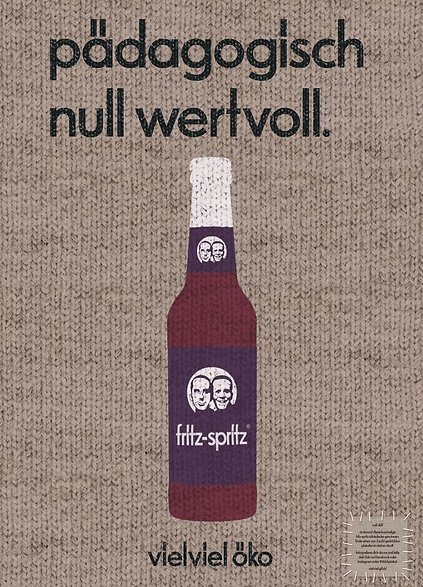 Werbeanzeige für die Bio-Schorle „fritz-spritz“ in einer Glasflasche mit violettem Etikett und dem bekannten Logo mit zwei Gesichtern. Darüber steht in schwarzer Schrift „pädagogisch null wertvoll.“, darunter der Slogan „vielviel öko“. Im unteren rechten Bereich befinden sich zwei Bio-Siegel. Hintergrund ist ein Strick-Look.
