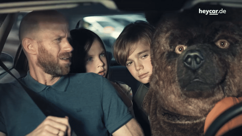 In einem Auto sitzt eine Familie mit einem Bären. Der Ausschnitt ist als Teaser gedacht und soll zum Klick animieren. 